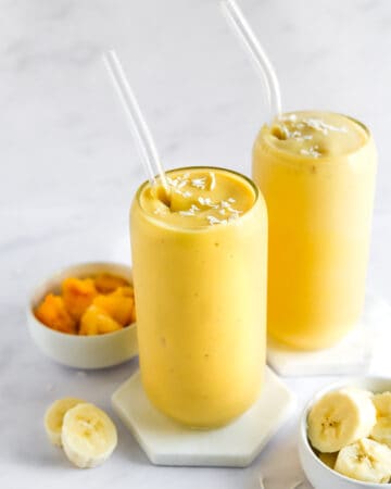 Two glasses filled with a mango smoothie with straws in the glasses.