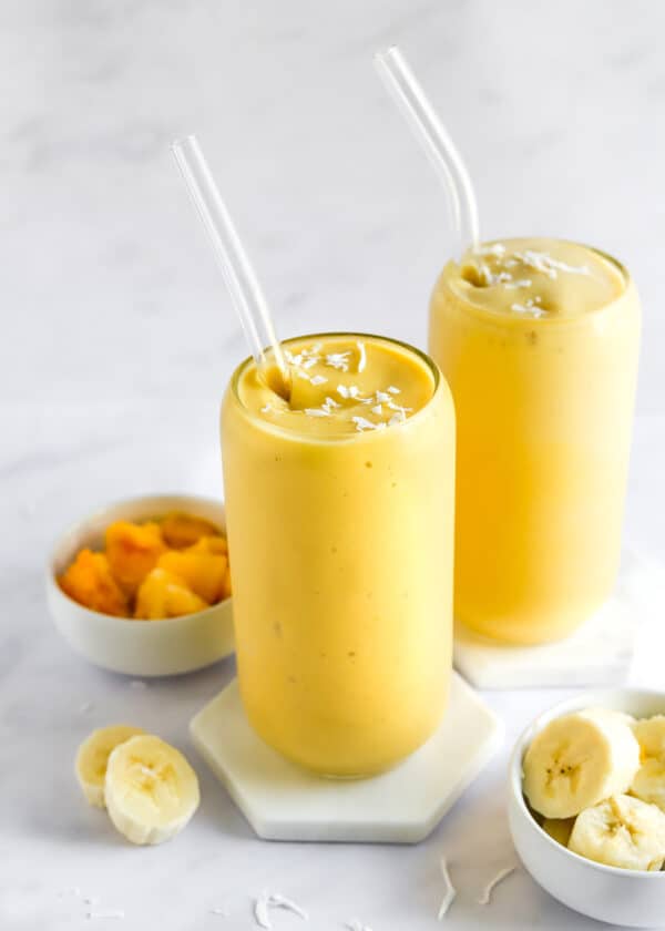 Two glasses filled with a mango smoothie with straws in the glasses.