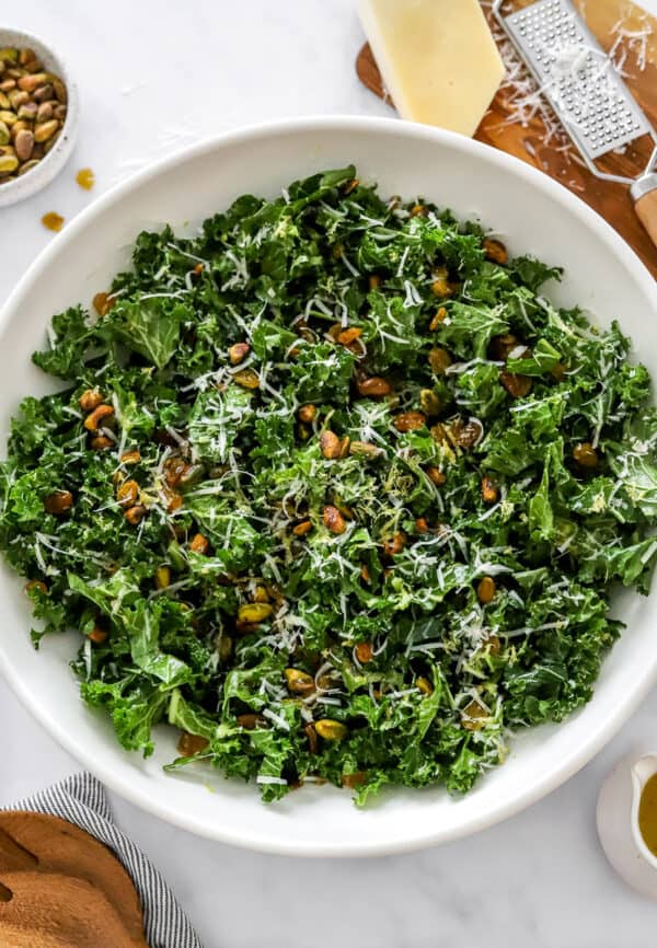 Chopped kale salad with nuts and shredded parmesan cheese on top of it with more parmesan and nuts behind it.