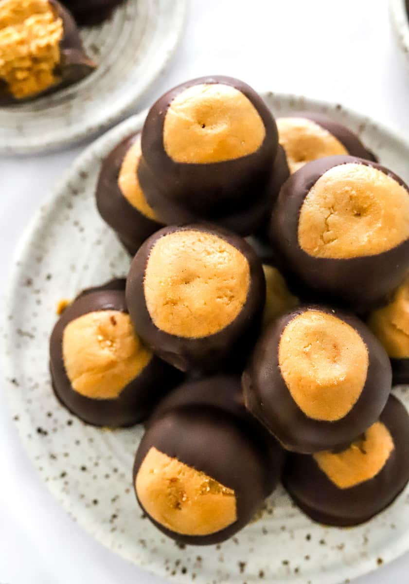 Pile of peanut butter buckeye balls on a plate with a bowl of peanut butter in front of them.