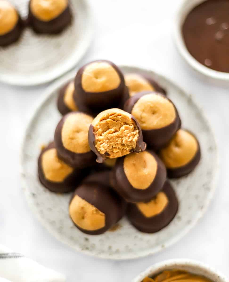 A plate filled with chocolate dipper peanut butter balls with more on a plate behind it and a bowl of melted chocolate behind it. 