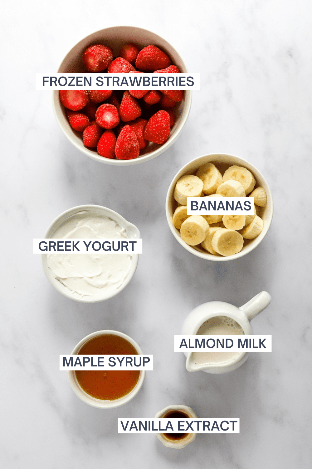 Ingredients for strawberry banana smoothie in bowls with labels over each ingredient. 