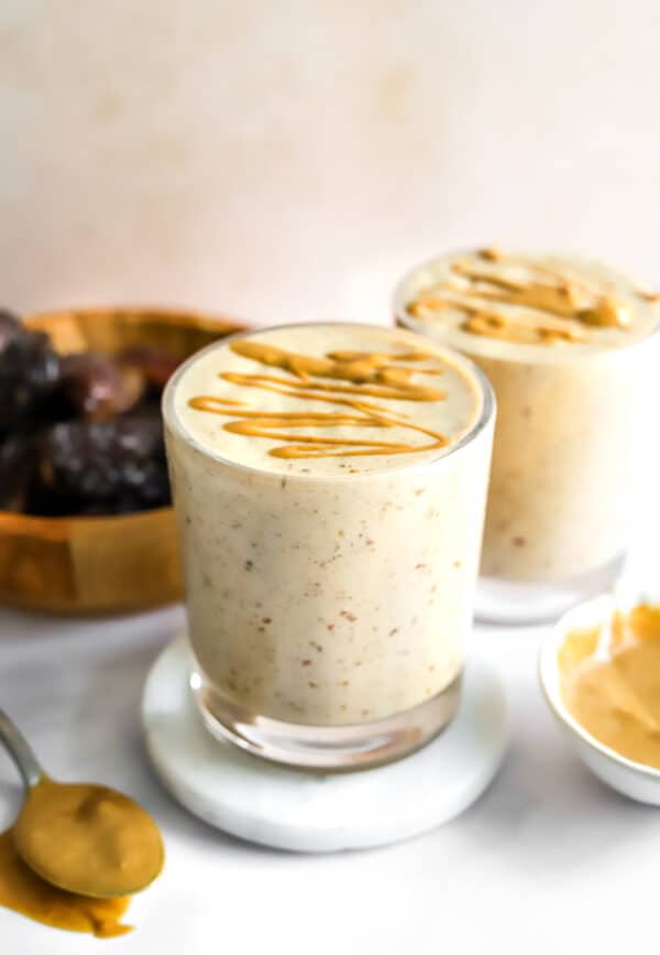 Two date shakes topped with a drizzle of peanut butter with a bowl of whole dates next to it.