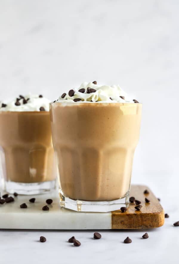 Chocolate protein shake in two glassed topped with whipped topping and chocolate chips.