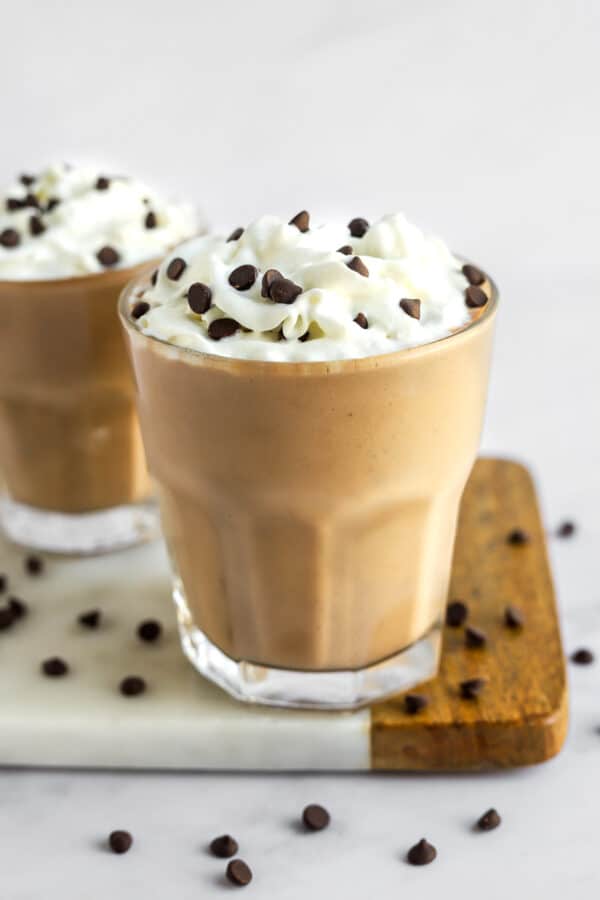 Chocolate shake in a glass with whipped cream and chocolate chips on top with another shake behind it.