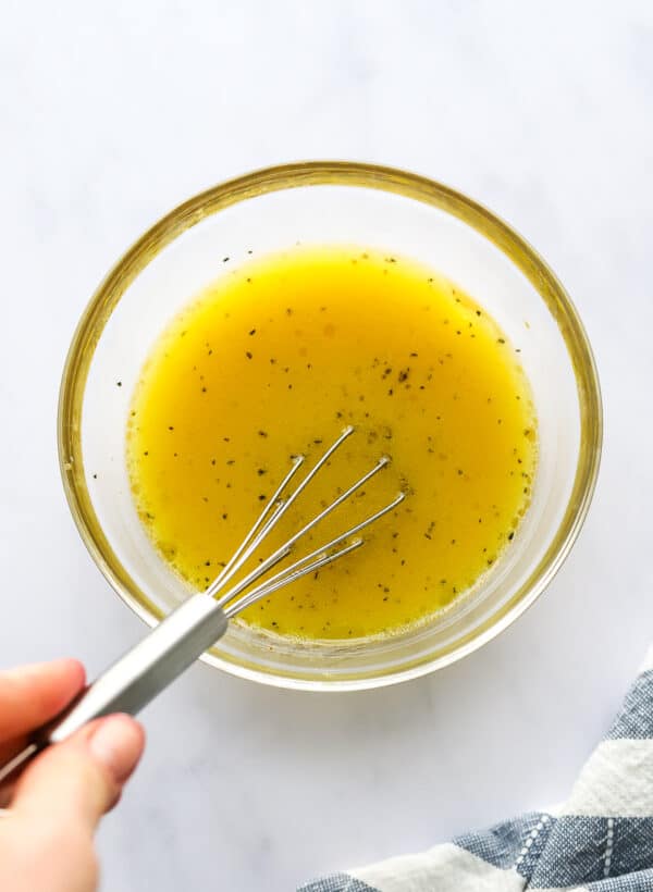 Hand mixing a citrus dressing in a glass bowl with a blue and white striped towel in front of it.
