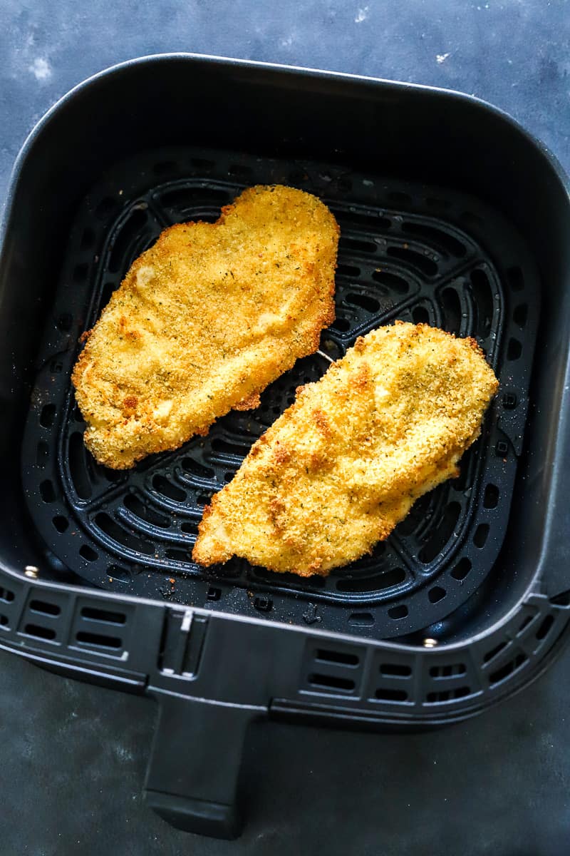 Two gold pieces of breaded chicken in a black air fryer basket.