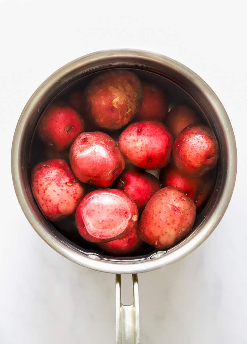 Raw red potatoes in a silver pot covered in water.