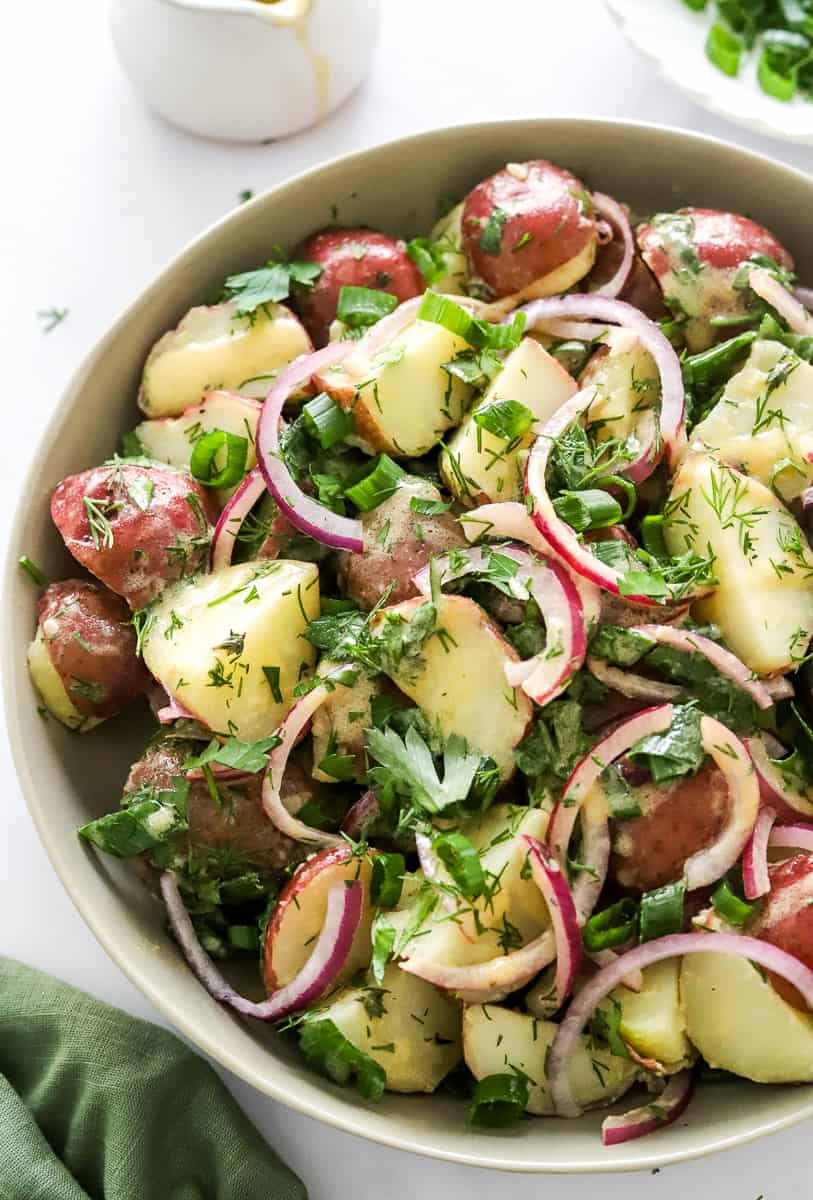 Bowl filled with herby, mustard red potato salad with a green linen in front of it.