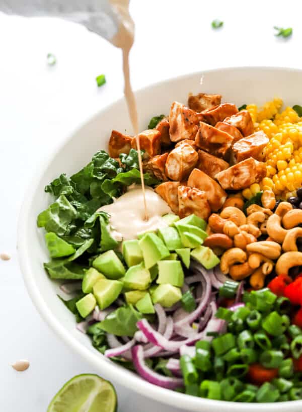 Pouring bbq dressing over a bowl filled with a veggie and chicken salad.