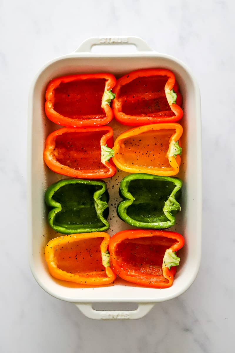 Different color bell peppers sliced in half in a white baking dish.