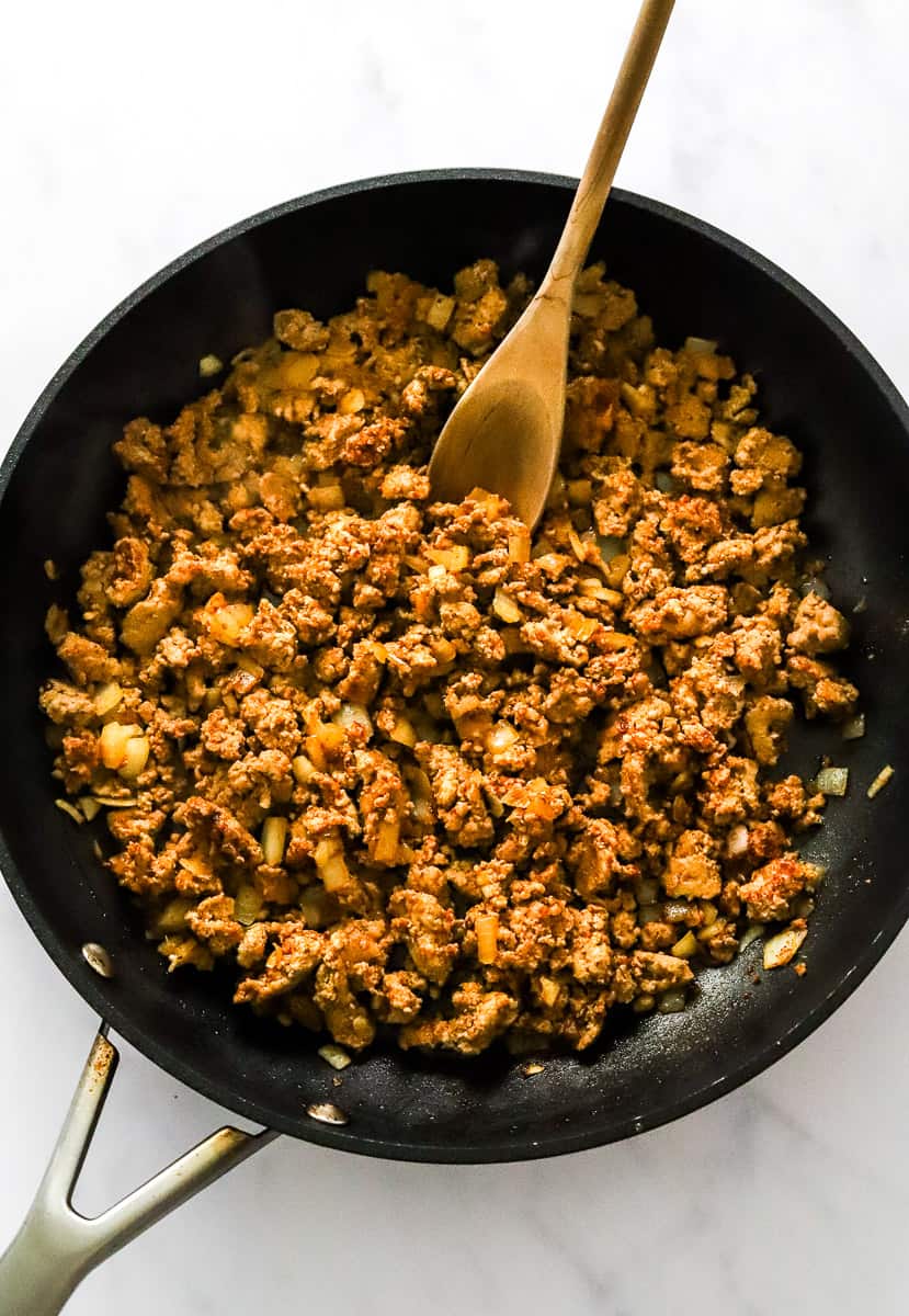 Cooked ground meat in a black skillet with a wooden spoon in the skillet.