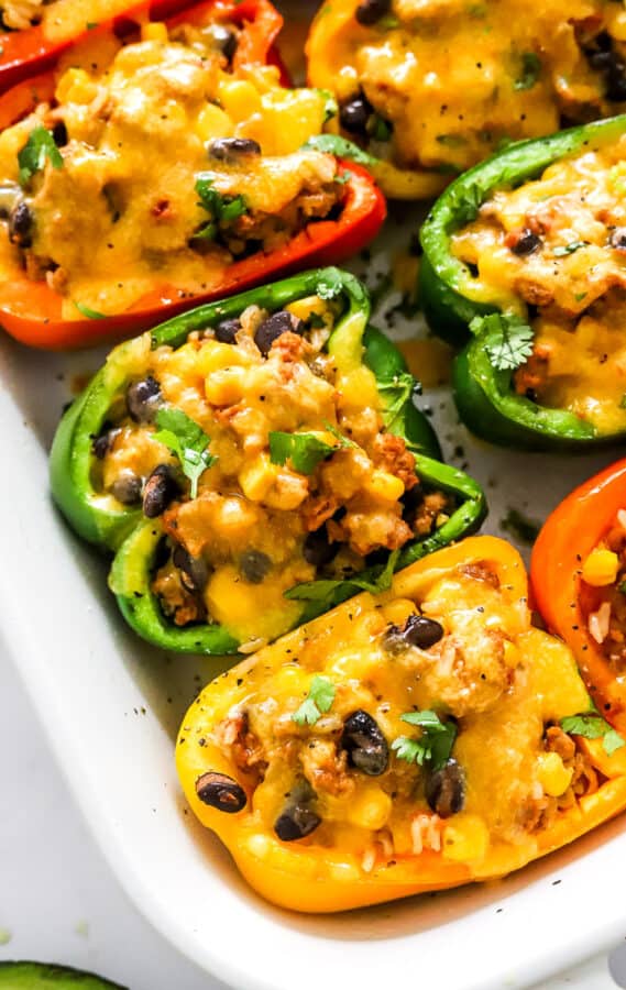 Green, orange, and red tacos stuffed bell peppers in a white dish topped with melted cheddar cheese.