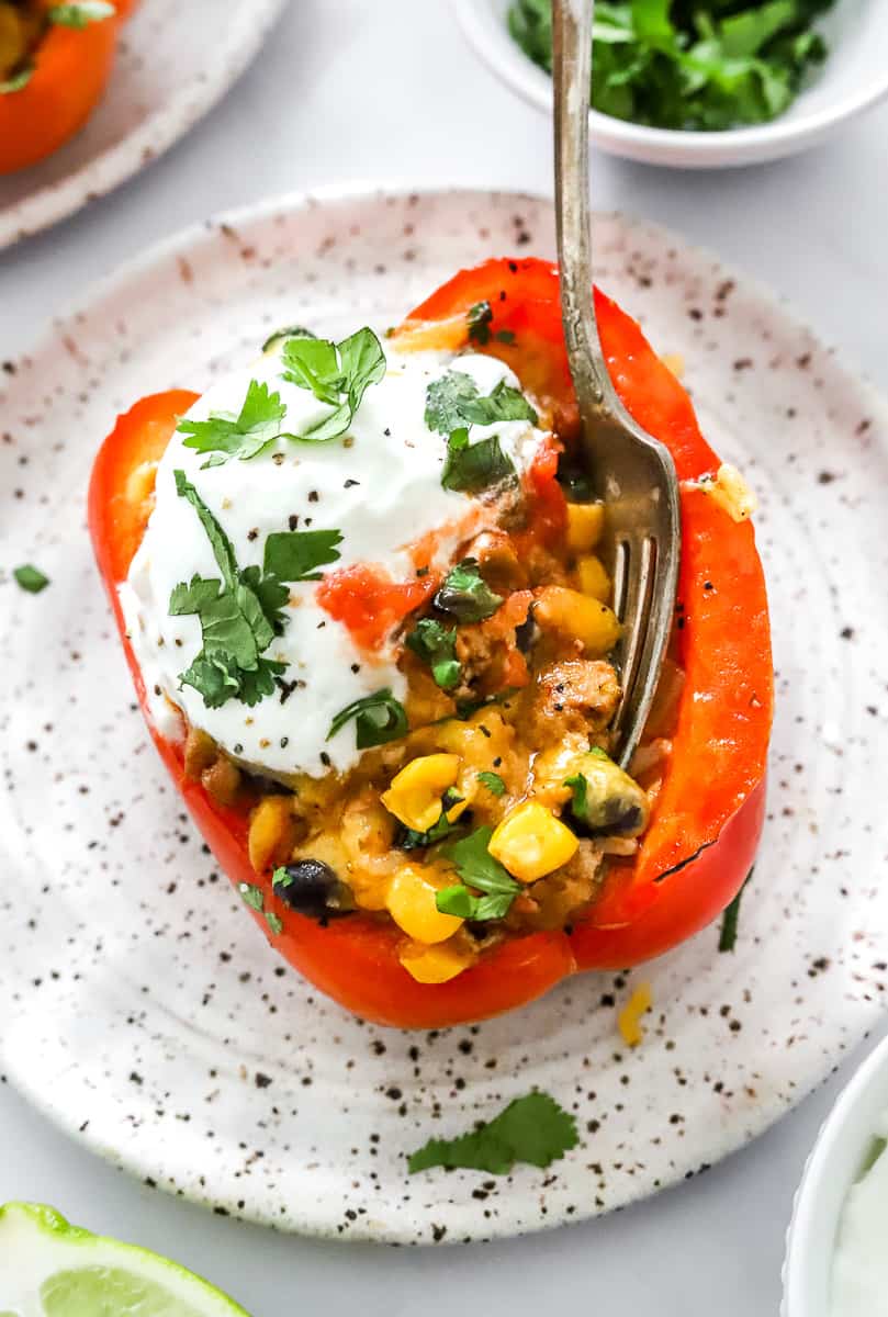 Single stuffed red bell pepper on a plate topped with greek yogurt and cilantro with a fork in the pepper.
