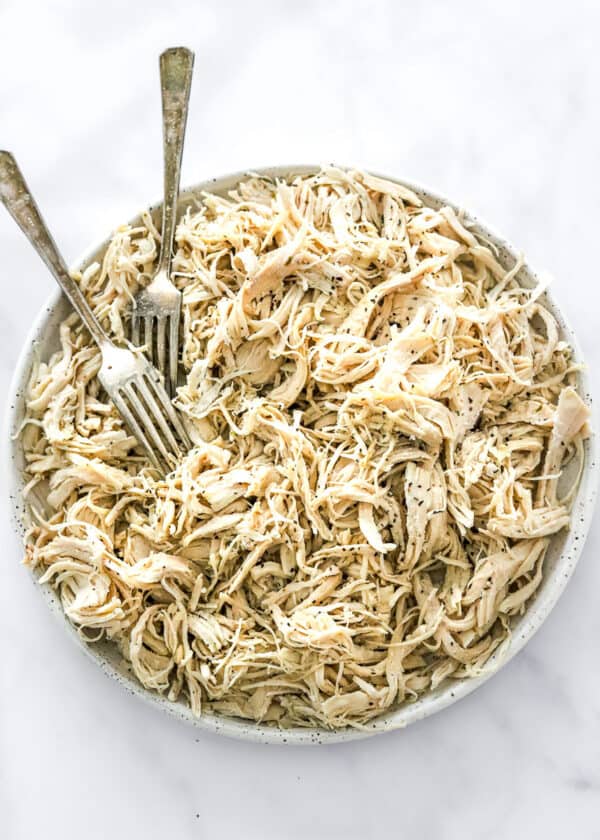 A lot of shredded chicken breast on a plate with two forks on the plate with it.