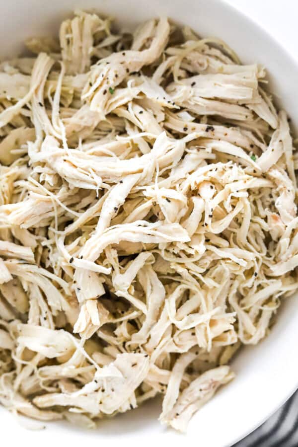 Close up of cooked shredded chicken breast in a white bowl.