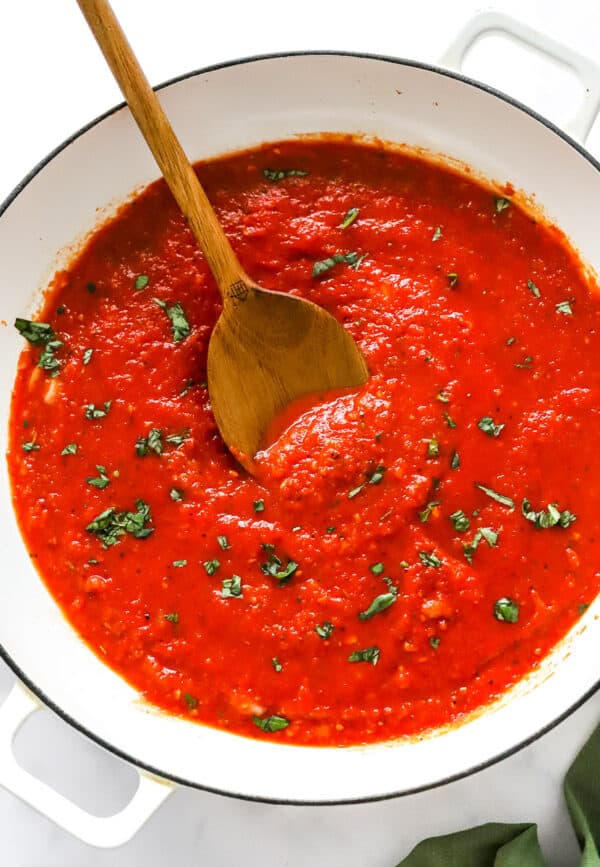 Pot filled whith cooked red sauce topped with green herbs with a wooden spoon in the pot.