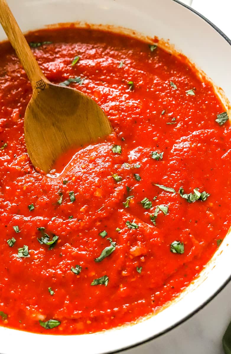 Round white pan filled with cooked tomato sauce with a wooden spoon in the pan.