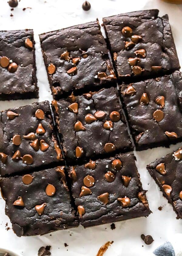 9 dark chocolate avocado brownies with chocolate chips on top, cut into squares on top of white parchment paper.