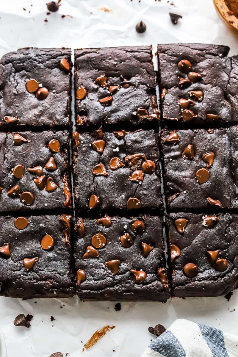 Cut chocolate avocado brownies next to each other in 3 rows with a blue and white linen in front of them.