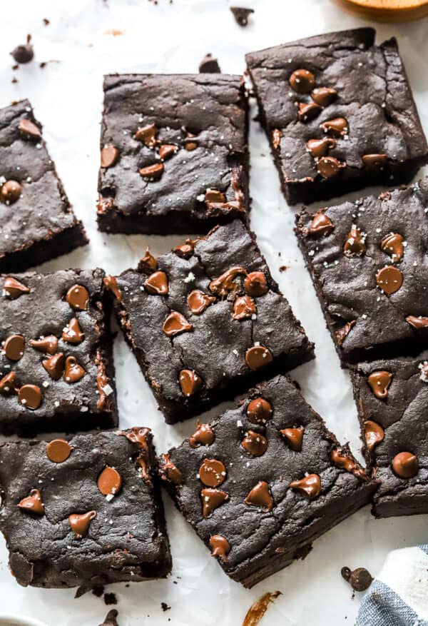 Cut avocado brownies on parchment paper with chocolate chips sprinkled around them.
