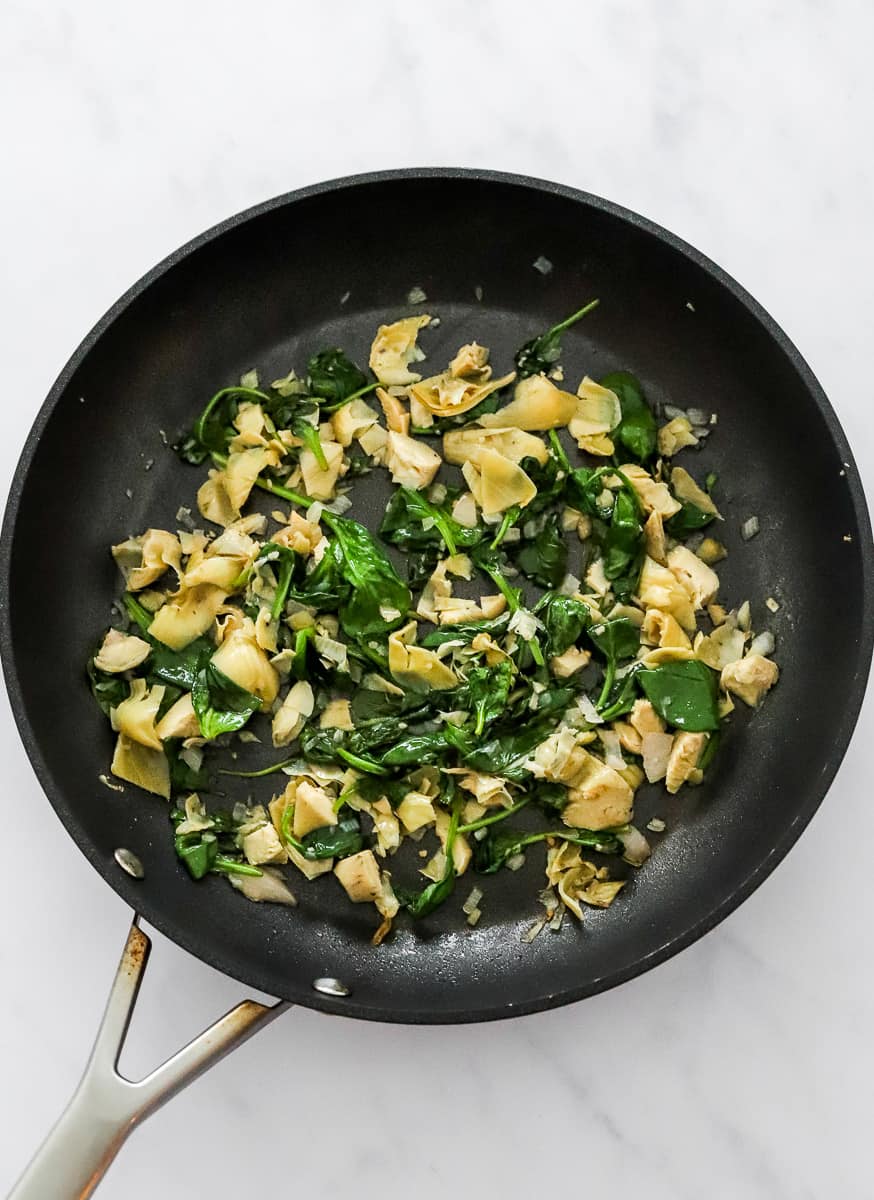 Cooked spinach, onions, garlic, and artichokes in a black skillet.