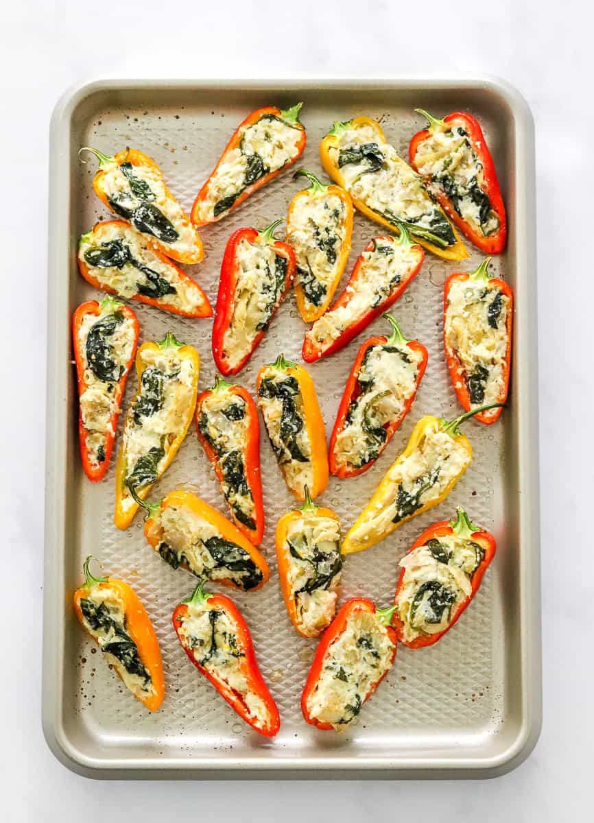 Gold baking sheet with a bunch of cheese stuffed mini peppers on it.