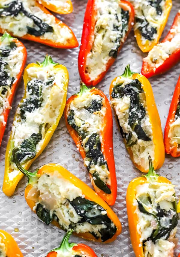 Close up of sweet small peppers filled with cheese, spinach and artichoke filling on a baking sheet.