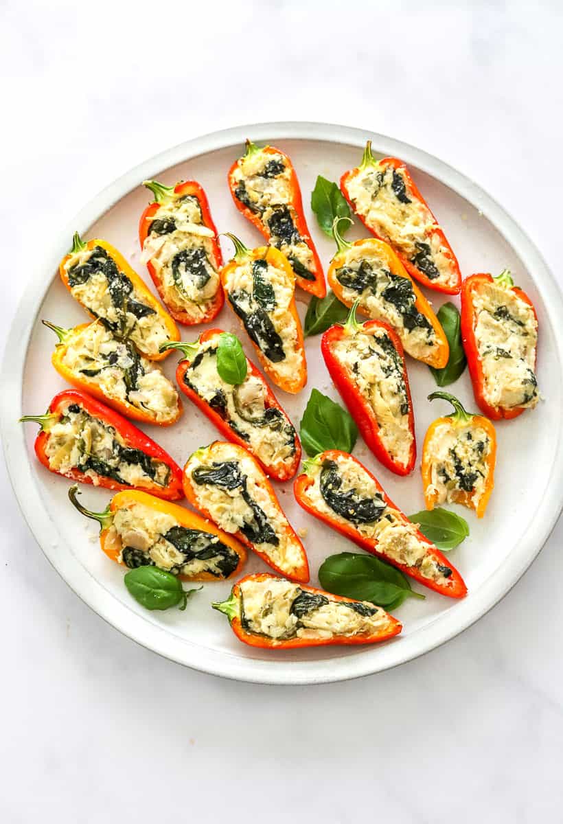 Round platter of mini stuffed red, yellow, and orange peppers filled with a cheesy, spinach filling.