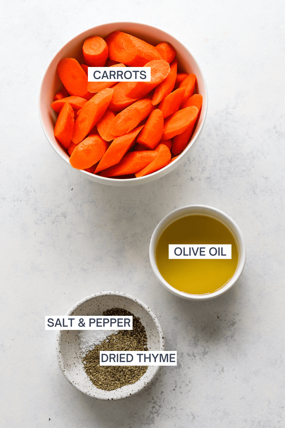 Bowl of cut carrots with a bowl of olive oil and a bowl of thyme, salt and pepper in front of it with labels over each ingredient. 