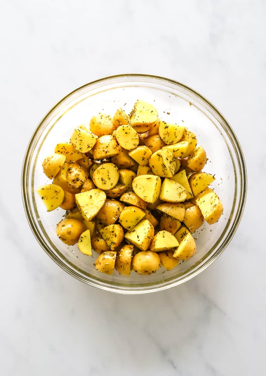 Round glass bowl filled with cut gold baby potatoes with seasoning on them.