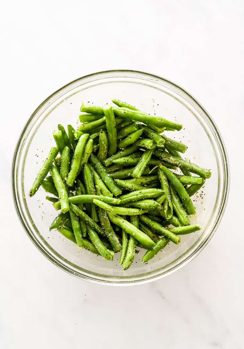 Round glass bowl filled with raw, cut, seasoned green beans.