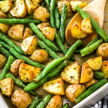 A wooden spoon on a baking sheet filled with crispy gold potatoes and cooked string beans.