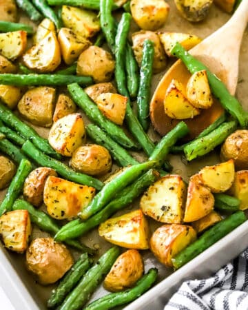 A wooden spoon on a baking sheet filled with crispy gold potatoes and cooked string beans.