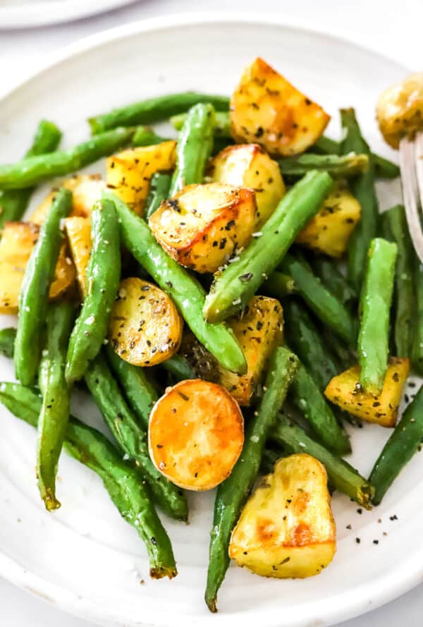 Close up of roasted green beans and crisp gold potatoes on a plate.