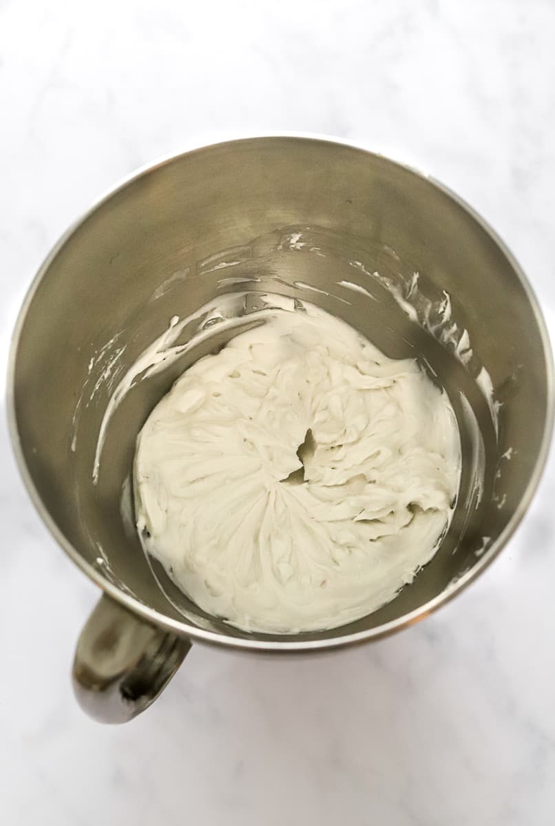 Whipped coconut cream in a silver mixing bowl with a handle.