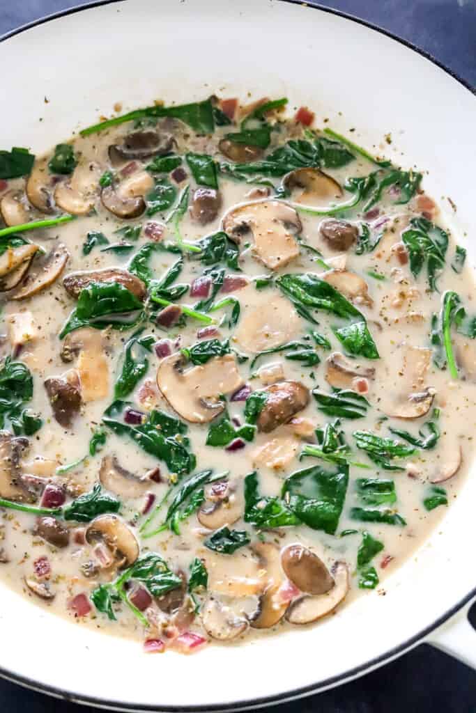 Creamy mushroom and spinach sauce in a round white pan. 