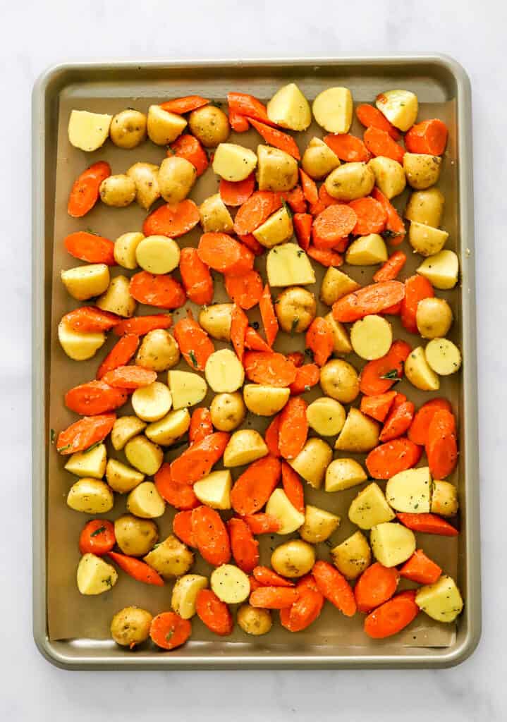 Seasoned cut pieces of carrots and potatoes on a baking sheet lined with brown parchment paper. 