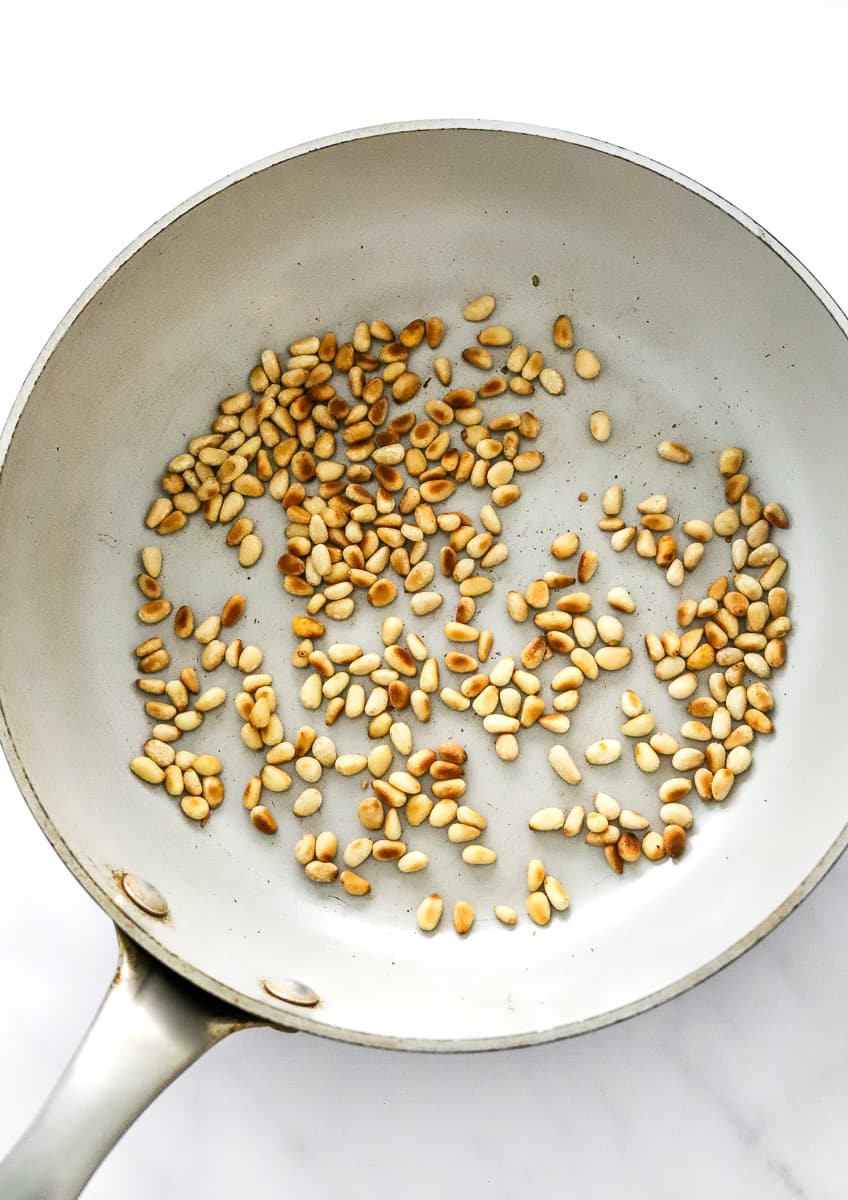 Pine nuts being toasted in a pan.
