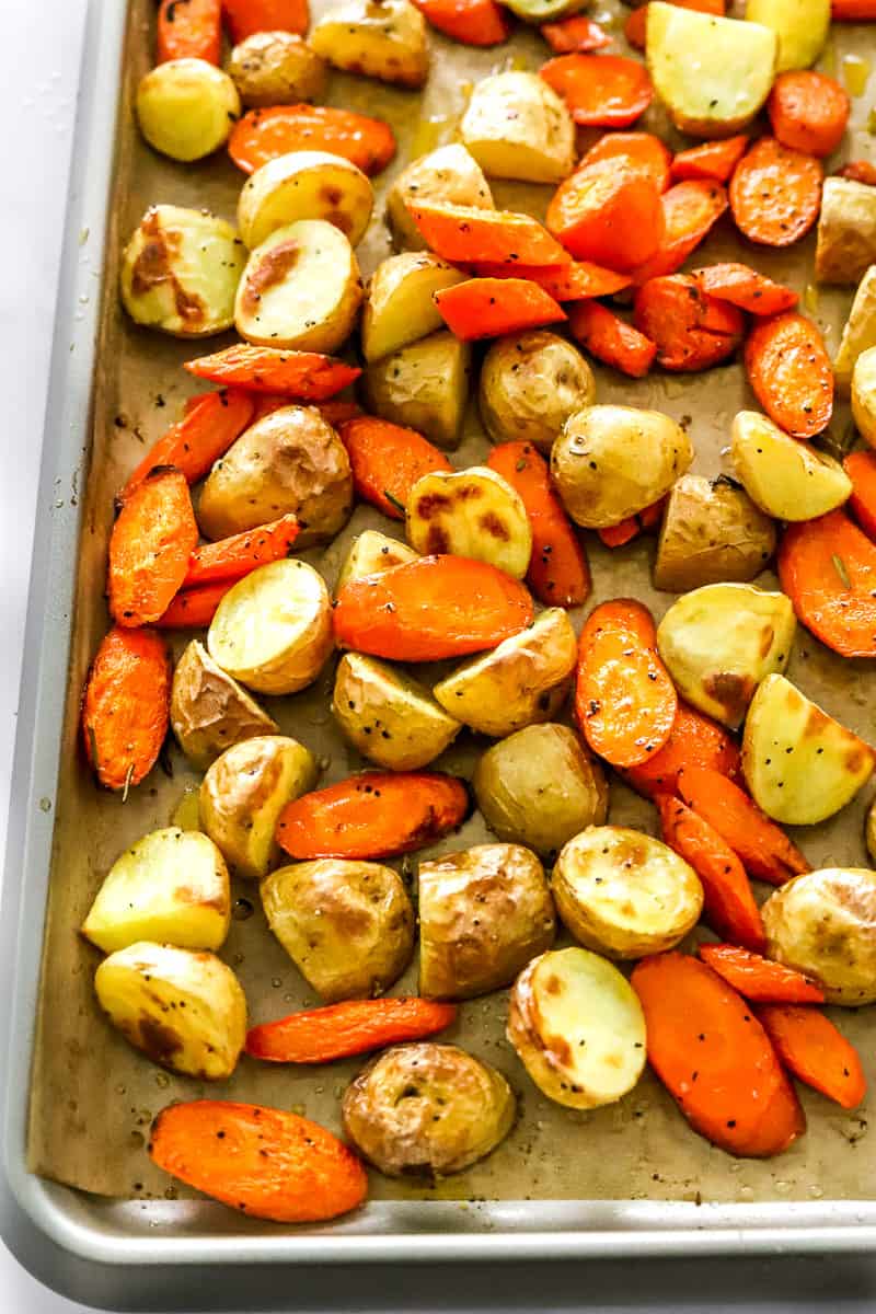 Baking sheet filled with golden roasted carrots and potatoes on top of brown parchment paper. 
