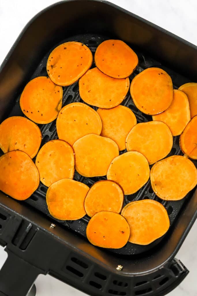 Uncooked, sliced sweet potatoes in a black air fryer basket. 