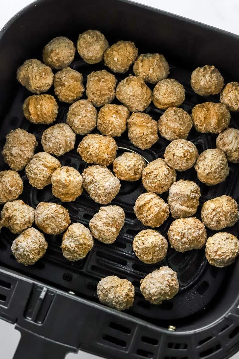 Frozen meatballs in a black air fryer basket.