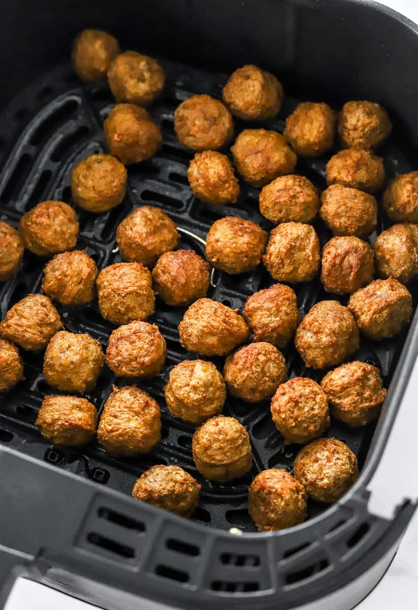 Golden brown cooked meatballs in an air fryer basket.