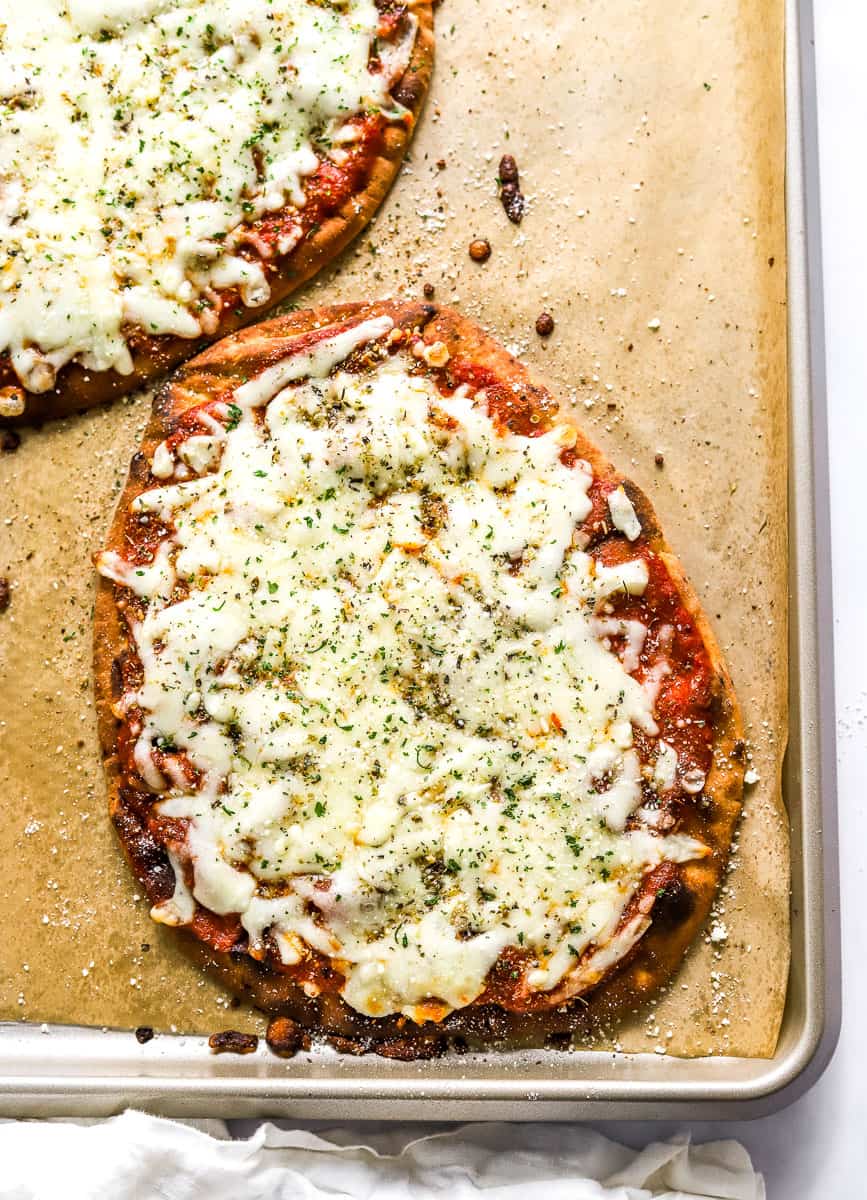 Cooked individual pizzas on a lined baking sheet with sauce and melted cheese on top of them.