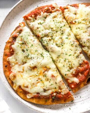 Golden cooked naan pizza topped with red sauce and cheese cut into large, rectangular pieces.