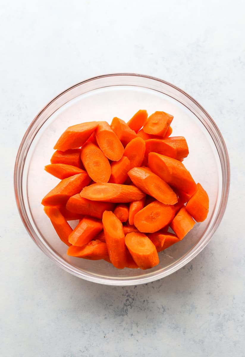 Glass mixing bowl filled with raw peeled and cut carrots. 