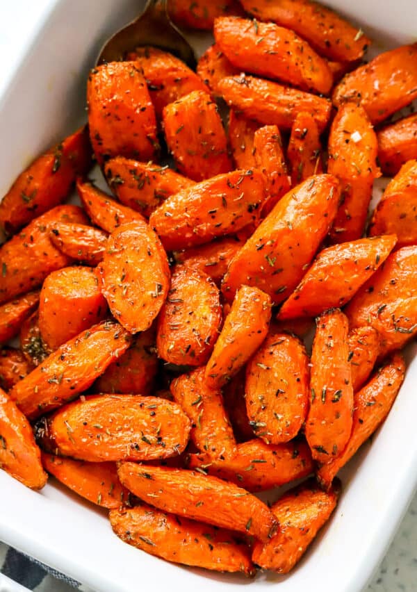 Cooked, golden carrots seasoned with thyme in a white serving dish.