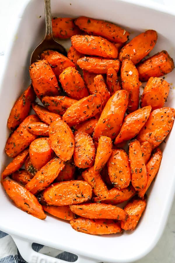 Rectangle baking dish filled with air fryer roasted carrots with a slier serving spoon in the dish and a striped linen in front of it.