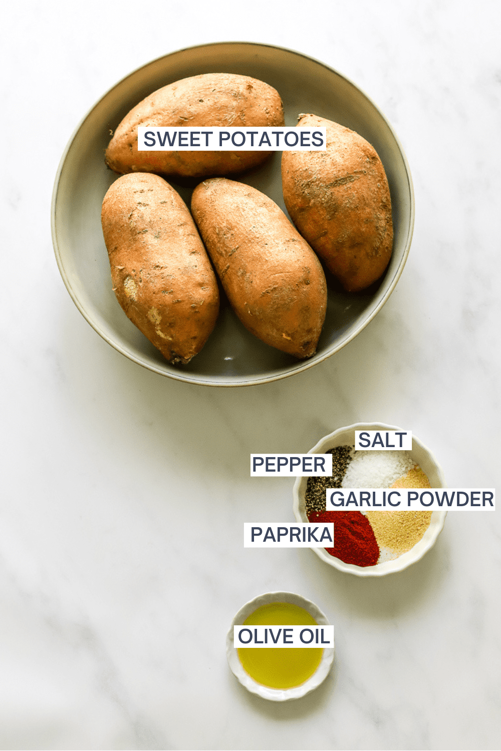Bowl of whole uncooked sweet potatoes with a bowl of spices and a bowl of olive oil in front of it with labels over each ingredient.