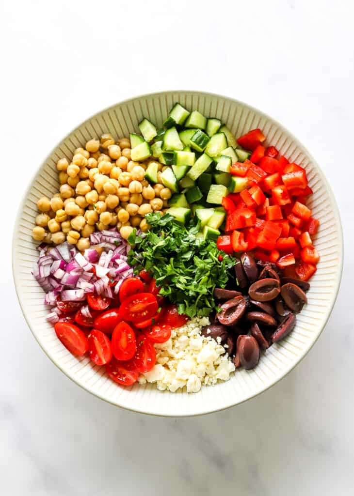 Chickpeas, chopped cucumber, chopped red bell pepper, chopped red onion, chopped parsley, sliced olives and feta cheese in a large salad bowl. 